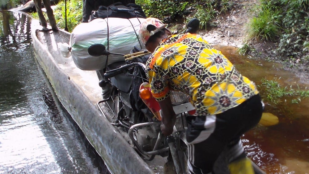 A boda (motorbike) driver loads his motorbike onto a canoe to cross a river