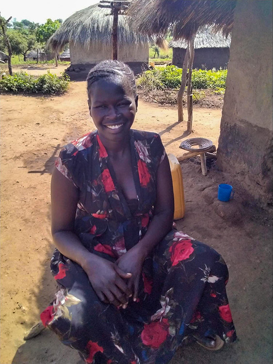 A photo of Anna sitting at Bidi Bidi. She is looking toward the camera and smiling.